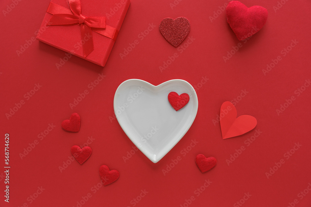 Ein weißer leerer Teller in Herzform auf einem roten Hintergrund. Valentinstag, Flat lay.