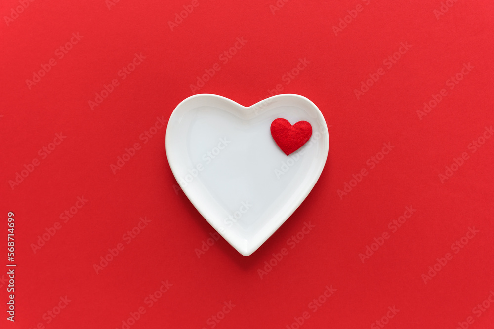 Ein weißer leerer Teller in Herzform auf einem roten Hintergrund. Valentinstag, Flat lay. Ein weißer leerer Teller in Herzform auf einem roten Hintergrund. Valentinstag, Flat lay.