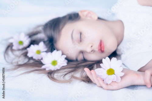 Close up portrait in pastel tones of a beautiful caucasian girl sleeping with daisy flowers in her long hair on white.