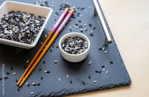 Wild black and white rice in white ceramic pots on a black background slate. Closeup
