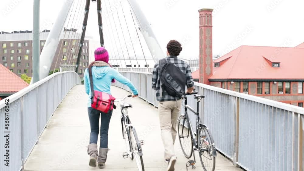 Wide shot bike commuters walking bikes on pedestrian bridge Wide shot bike commuters walking bikes on pedestrian bridge