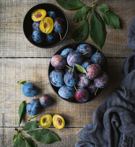 Top view of bowls of fresh picked plums on wooden background.