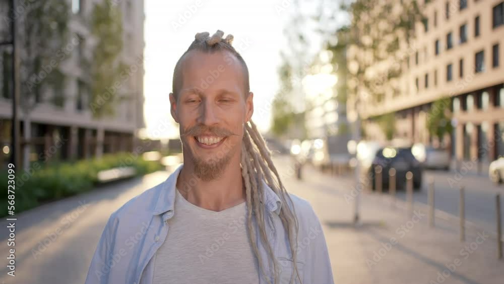 Portrait of young handsome smiling Caucasian guy hipster crazy man with beard dreadlocks looking at camera at city street. Male guy tourist travel face Expression, surprised human emotion people Portrait of young handsome smiling Caucasian guy hipster crazy man with beard dreadlocks looking at camera at city street. Male guy tourist travel face Expression, surprised human emotion people
