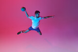 Top view. In a jump. Young man, professional handball player training, playing isolated over gradient pink background in neon light. Concept of sport, action, motion, championship, sportive lifestyle