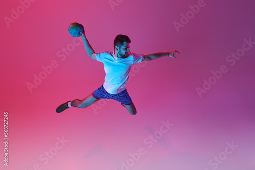 Top view. In a jump. Young man, professional handball player training, playing isolated over gradient pink background in neon light. Concept of sport, action, motion, championship, sportive lifestyle