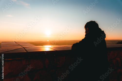 lonely young traveler looking at the cloudless sunset at a nice viewpoint on top of the mountain