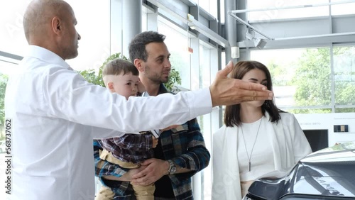 Happy young family chooses new car with manager at car dealership.