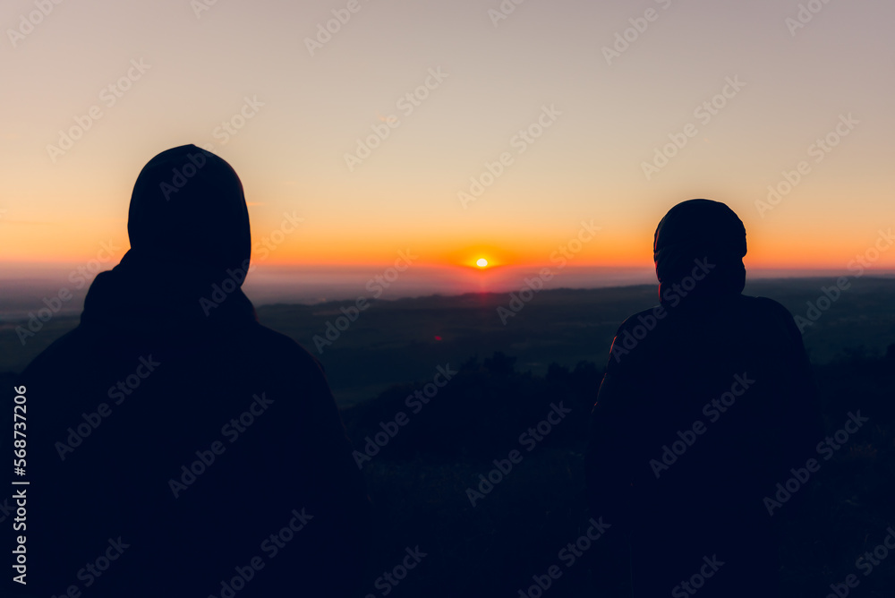 Couple of two boys watching the horizon and the sunset backlit together