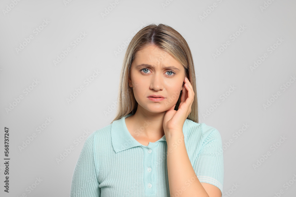 Young woman suffering from ear pain on light grey background Young woman suffering from ear pain on light grey background