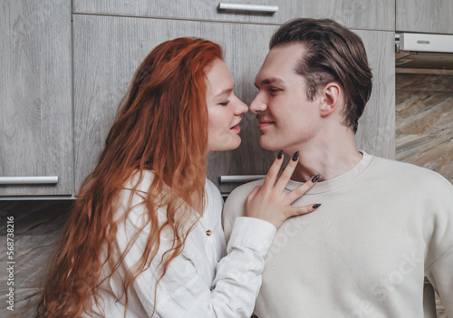 A romantic conversation in the kitchen of two lovers. Red-haired girl passionately touches her boyfriend. photo