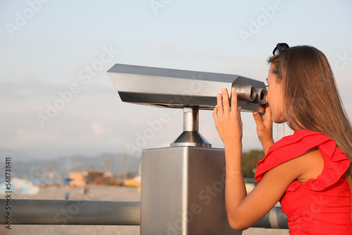 Young woman looking through tourist viewing machine at observation deck