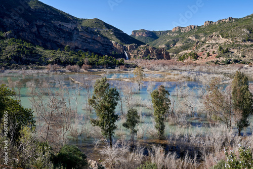 Beautiful landscape of the waterfall near the old town of Domeño on a rocky mountain full of vegetation and the Turia river with a lot of leafless groves and three trees in the foreground, in Valencia photo