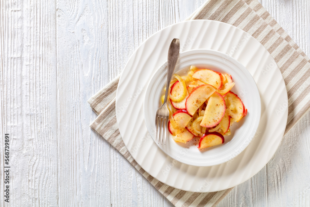 fried onion and red apple slices on white plate with fork on white wood table, horizontal view from above, free space fried onion and red apple slices on white plate with fork on white wood table, horizontal view from above, free space