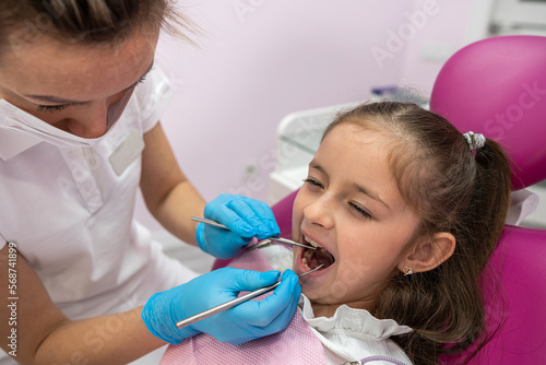  little patient grimaces during an examination of the oral cavity by a female dentist.