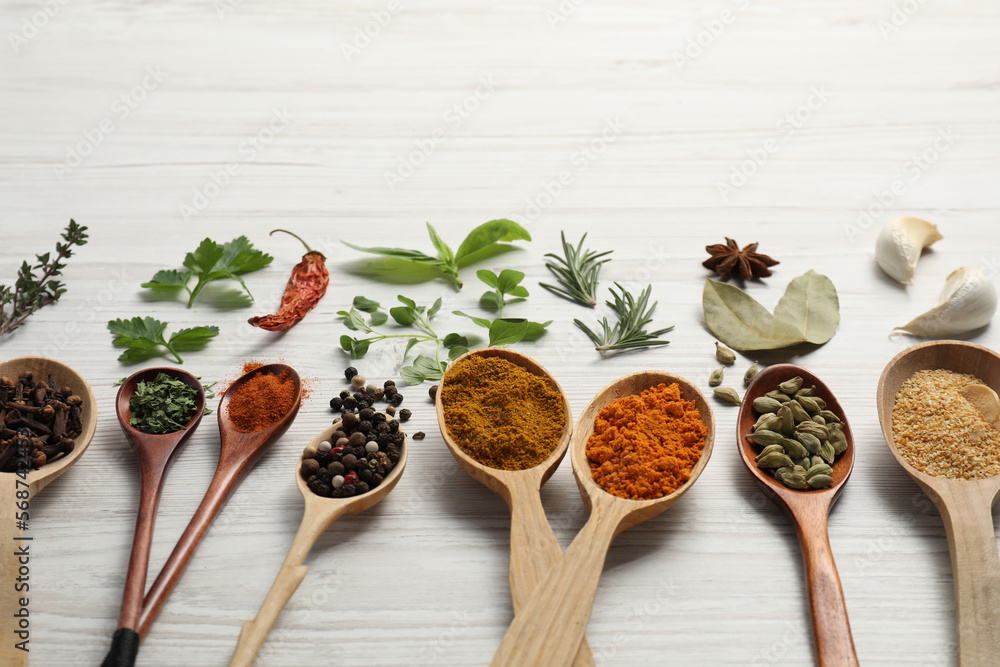 Spoons with different spices and herbs on white wooden table. Space for text Spoons with different spices and herbs on white wooden table. Space for text