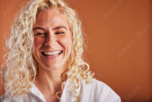Young blonde woman laughing with her eyes closed on an orange background photo