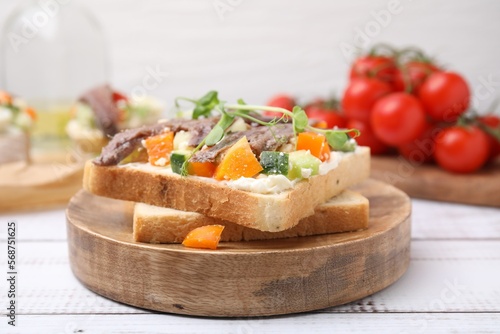 Delicious toasts with anchovies, cream cheese, bell peppers and cucumbers on white wooden table, closeup