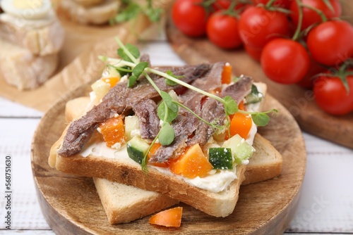 Delicious toasts with anchovies, cream cheese, bell peppers and cucumbers on white wooden table, closeup