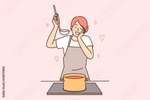 Happy housewife woman cooks soup standing at stove with saucepan and tastes after adding spices