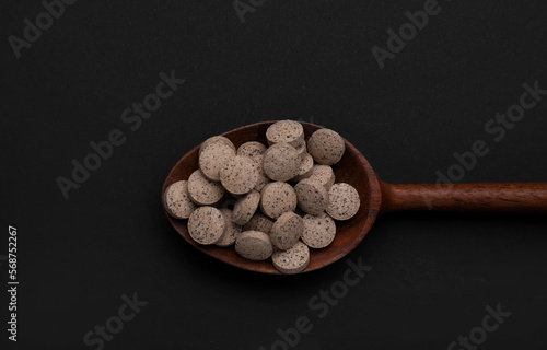 Wooden spoon of brewer`s yeast tablets on black background, top view photo