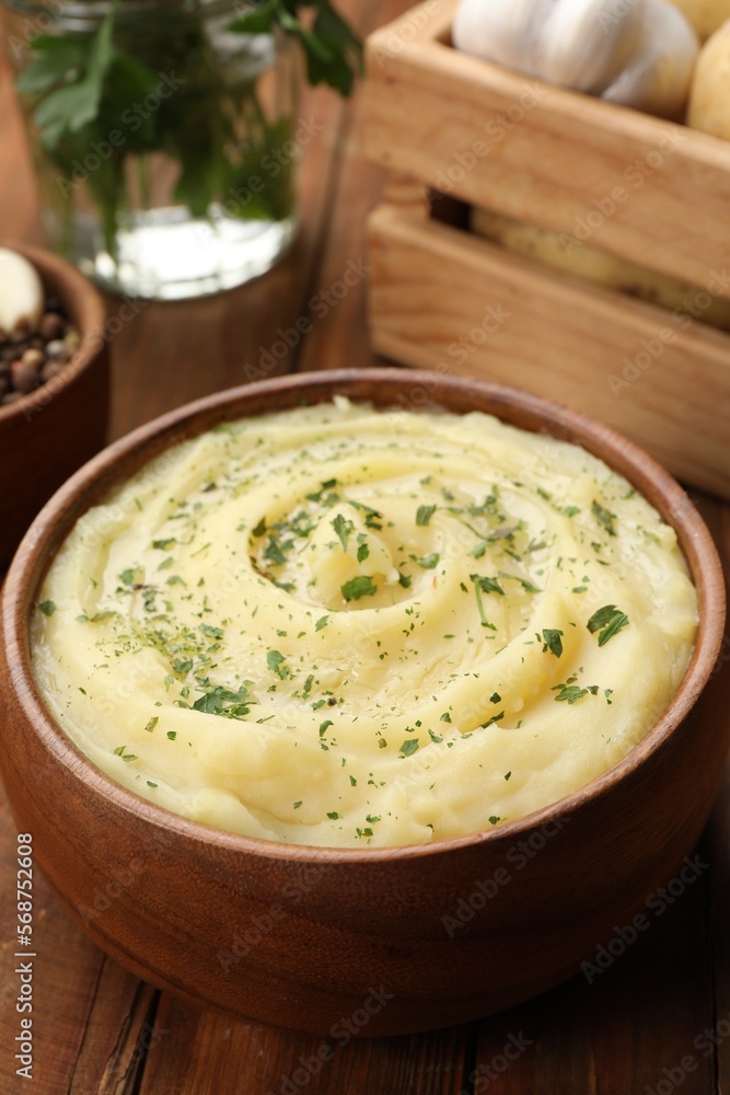 Bowl of tasty mashed potato with greens, garlic and pepper on wooden table, closeup