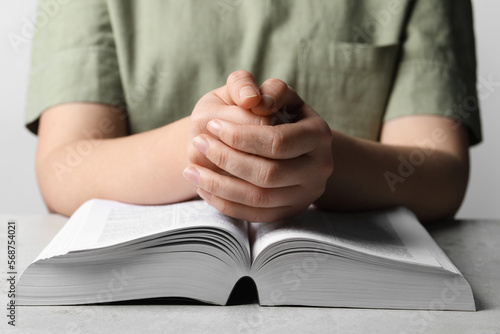 Woman holding hands clasped while praying over Bible at grey textured table, closeup