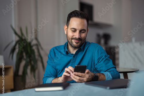 Adult businessman typing on a mobile phone, sitting in front of the laptop, indoors.
