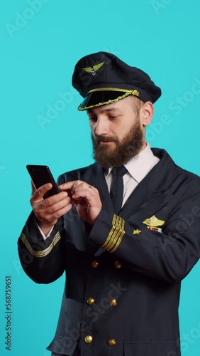 Vertical video: Young pilot reading good news on smartphone app, using onlien website and feeling happy about achievement. Male airline captain celebrating success on mobile phone, wearing uniform. photo