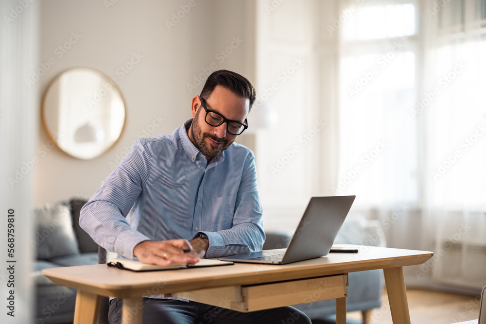Focused man writing notes in the notebook, sitting in front of the laptop at the office. Focused man writing notes in the notebook, sitting in front of the laptop at the office.