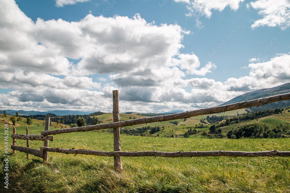 wooden fence in the field on the background of mountains and cloudy sky.