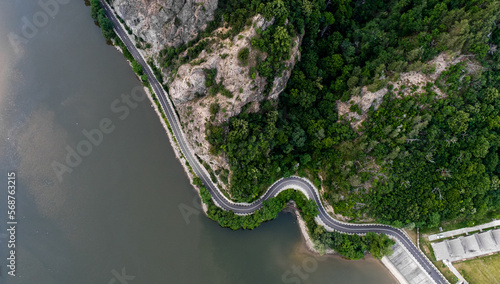 Aerial birds eye view of a cliff coast road between mountains and a river in the dusk. Amazing roads of the world. Transportation industry.