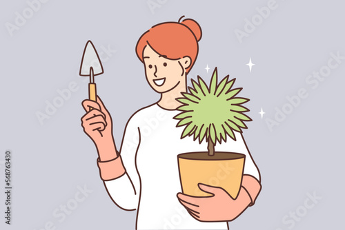 Woman caring for house plant in pot holds shovel to replace earth or transplant flower