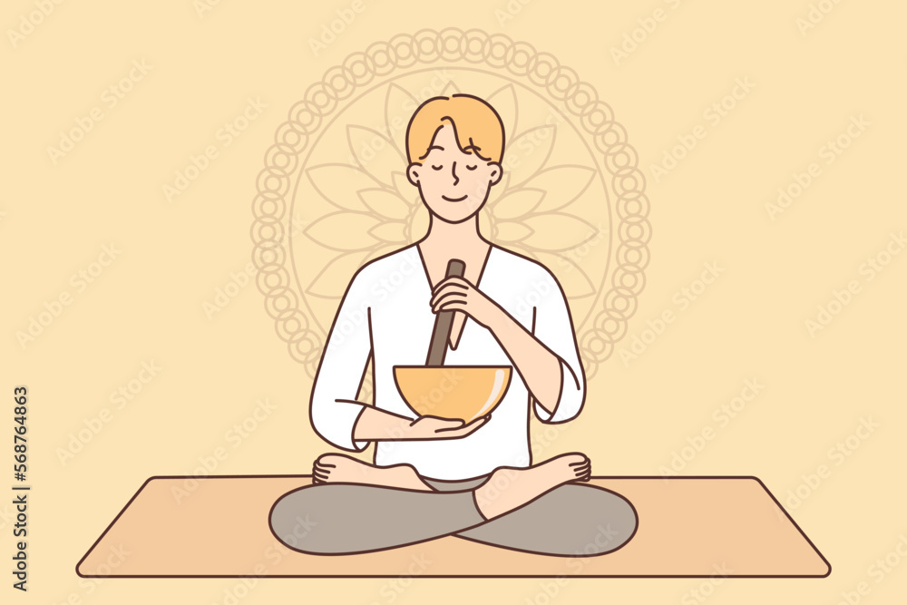 Meditating man sitting in lotus position on yoga mat using bowl to perform ancient ritual Meditating man sitting in lotus position on yoga mat using bowl to perform ancient ritual