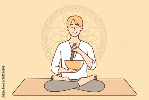 Meditating man sitting in lotus position on yoga mat using bowl to perform ancient ritual