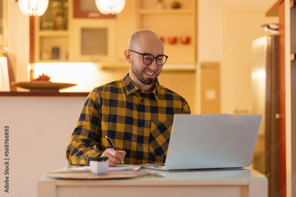 Fototapeta premium Portrait of young Caucasian man wearing glasses smiling and working on laptop. Worker using computer. Concept of remote work and freelance