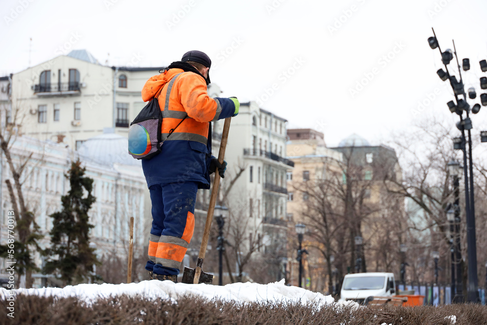 custom made wallpaper toronto digitalWorker in uniform cleaning snow on winter street. Man with a shovel standing against city buildings