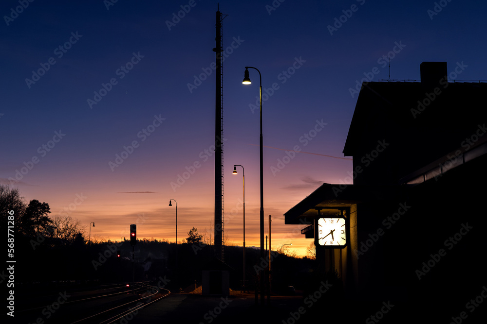 Evening photo of an empty train station. Colorful sky and railway lights. The clock reads 5:40 p.m. - obrazy, fototapety, plakaty 