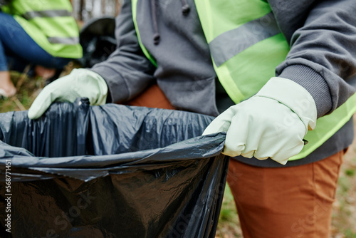Closeup image of volunteer holding big trash bag for garbage collected in city park photo