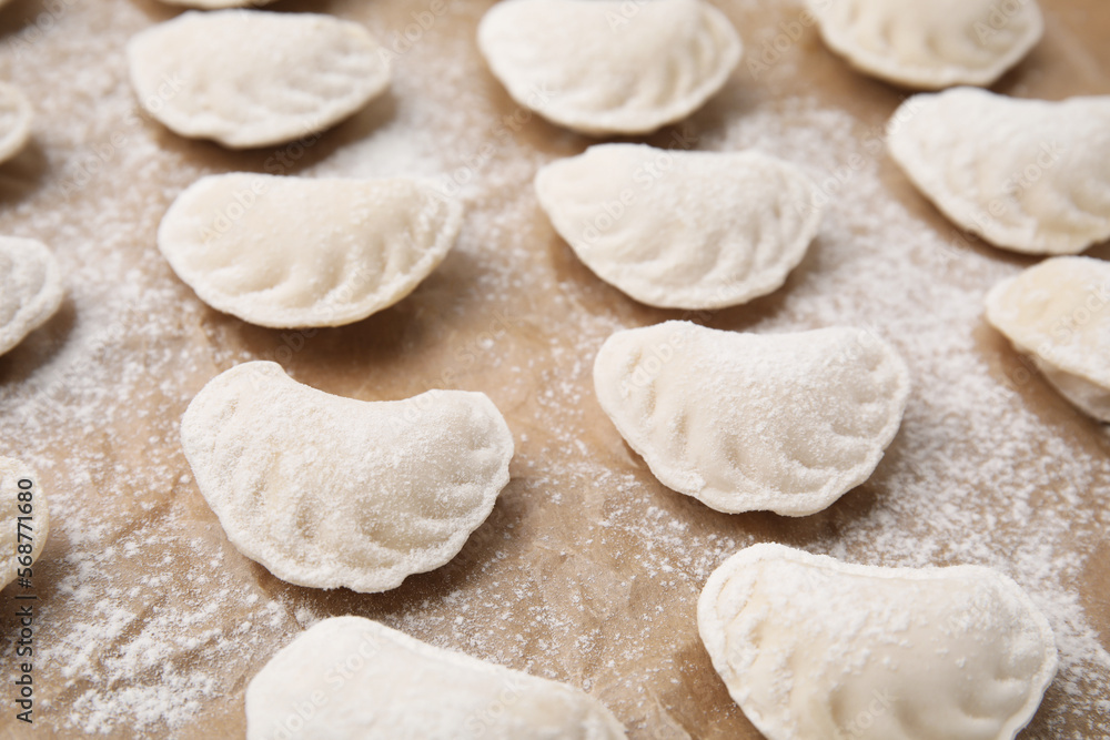 Raw dumplings (varenyky) with tasty filling and flour on parchment paper, closeup view