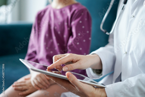 Doctor woman and kid patient at home. The pediatrician uses a tablet computer, close up. Medicine, healthcare concepts.