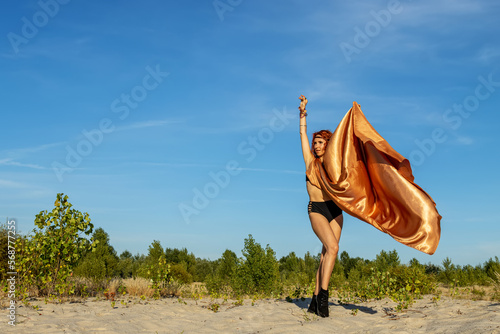 Young woman model outdoors on a summer day. Girl in a cape of gold fabric. Fashion and Style.