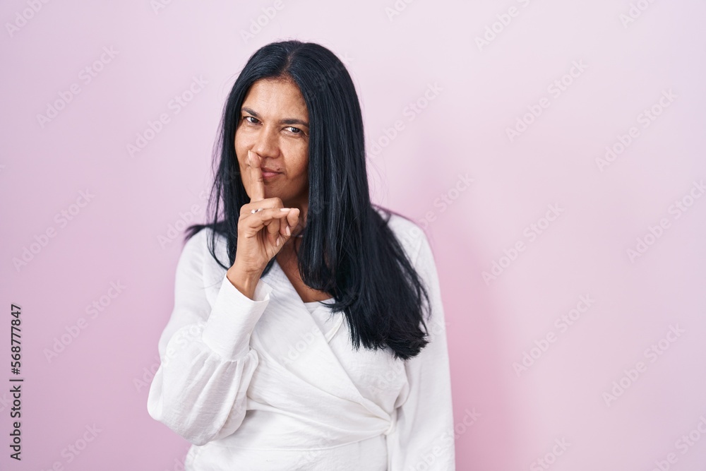 Mature hispanic woman standing over pink background asking to be quiet with finger on lips. silence and secret concept. Mature hispanic woman standing over pink background asking to be quiet with finger on lips. silence and secret concept.