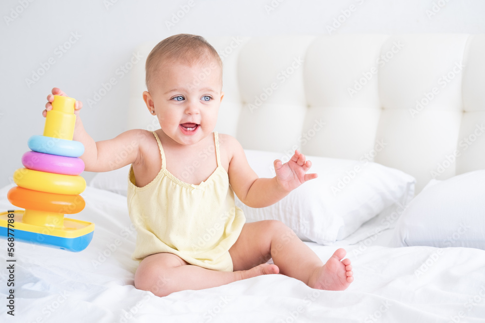 funny baby girl in yellow bodysuit playing with plastic toy children pyramid on bed
