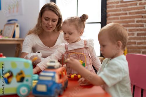 Teacher with boy and girl playing with toys sitting on table at kindergarten