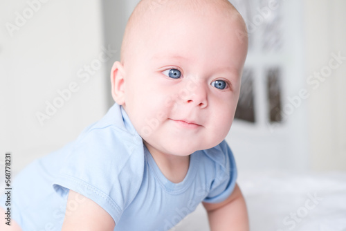 Photography portrait of smiling baby boy with big blue eyes in bodysuit on white bedding