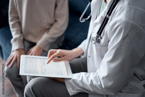 Doctor woman and kid boy patient at home. The pediatrician using tablet computer while filling up medical records, close up. Medicine, healthcare concept