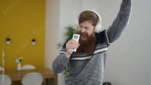 Young redhead man listening to music singing song at home photo