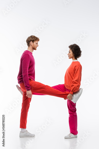 side view of multiethnic couple in magenta color clothes showing h letter with legs on white background.