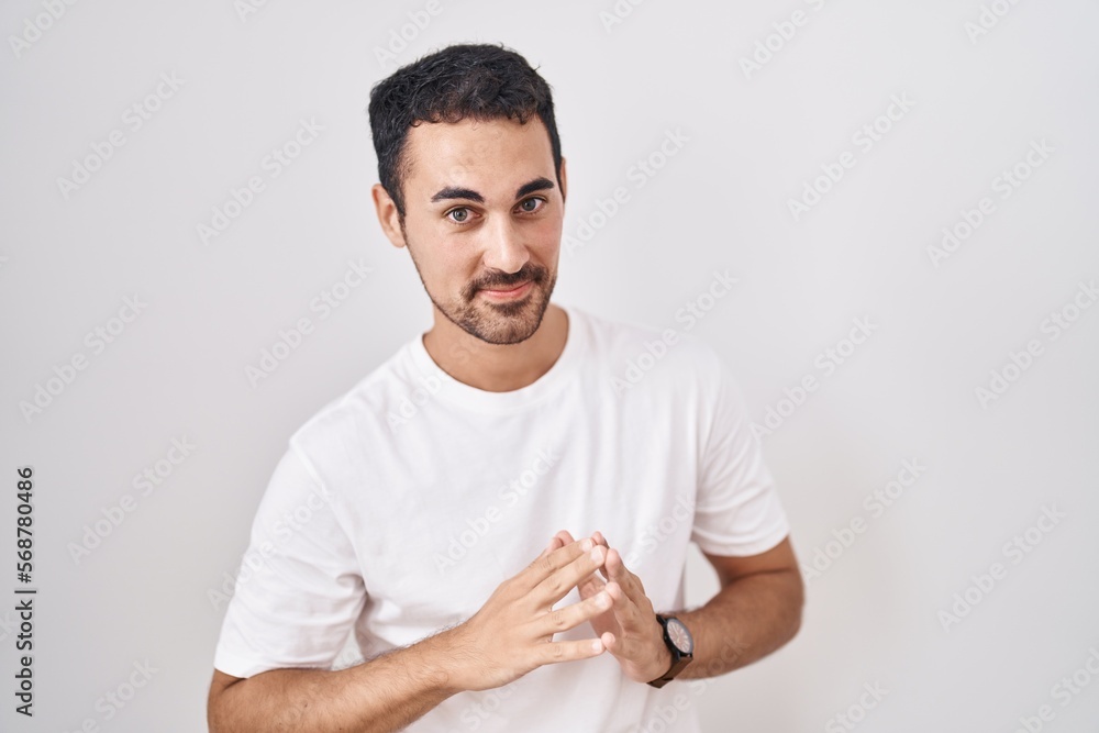Handsome hispanic man standing over white background hands together and fingers crossed smiling relaxed and cheerful. success and optimistic Handsome hispanic man standing over white background hands together and fingers crossed smiling relaxed and cheerful. success and optimistic