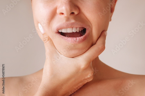 Cropped shot of a young woman suffering from jaw pain holding her chin isolated on a beige background. Inflammation of cervical lymph nodes, Diseases of ENT organs, facial, trigeminal nerve, toothache